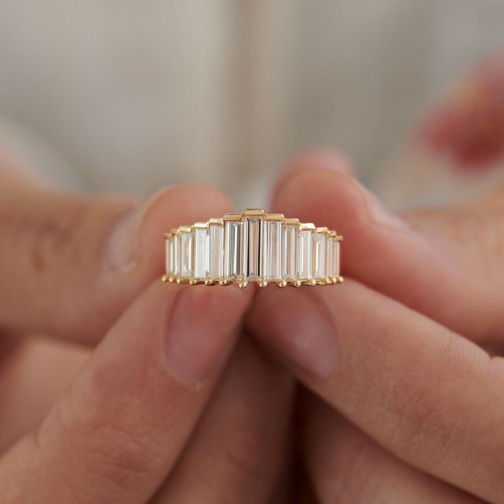 a woman's hand holding a gold ring with three baguettes