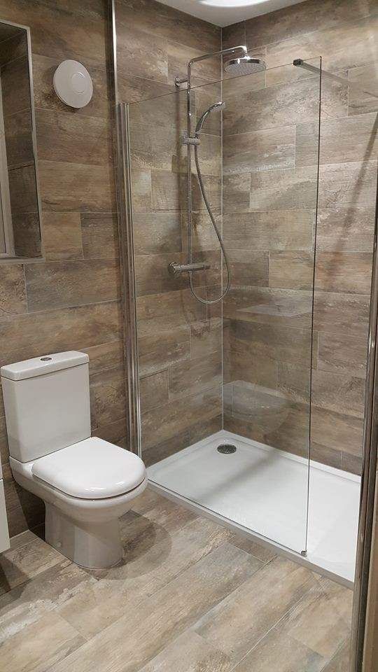 a bathroom with a walk in shower next to a white toilet and wooden flooring