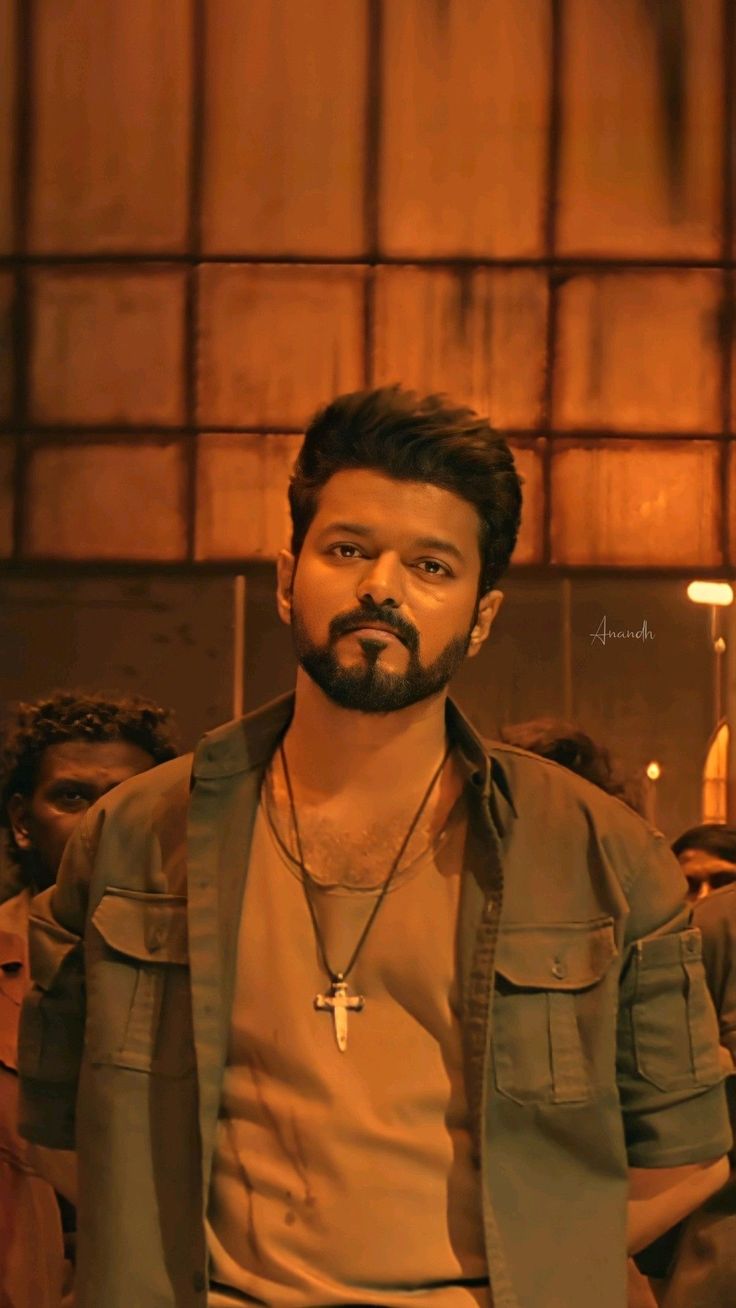 a man with a cross necklace standing in front of a group of people wearing brown shirts