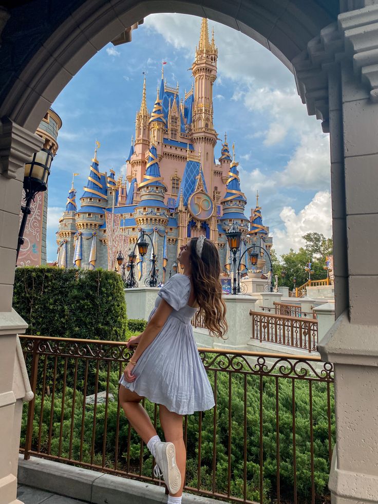 a woman standing in front of a castle with her legs crossed and looking at the sky