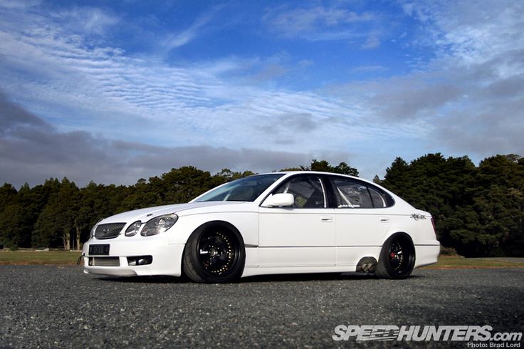 a white car is parked on the side of the road near some trees and clouds