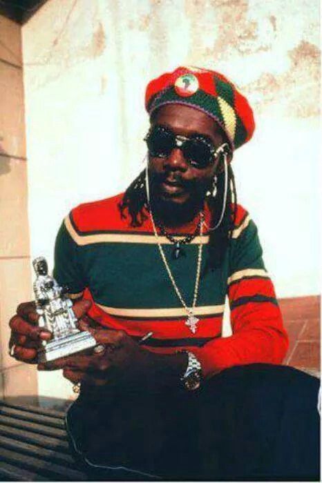 a man sitting on top of a bench holding a silver object in his hand and wearing a red hat