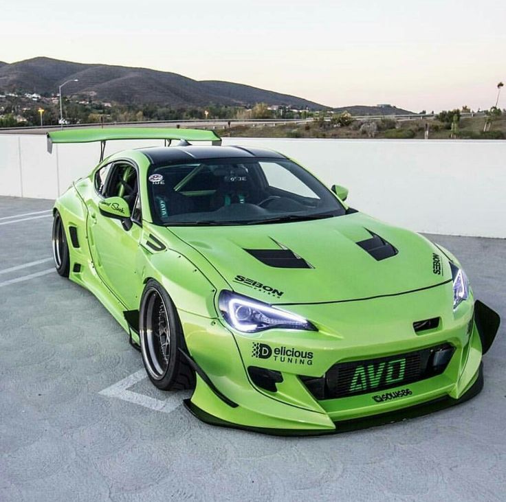 a bright green sports car parked in a parking lot next to a white wall and mountains