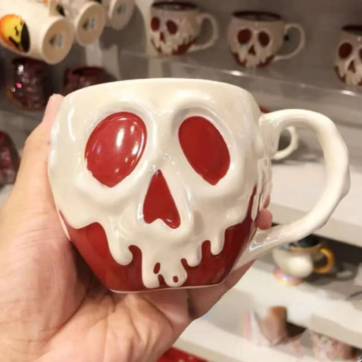 a hand holding a coffee cup with a skull painted on the side and red eyes