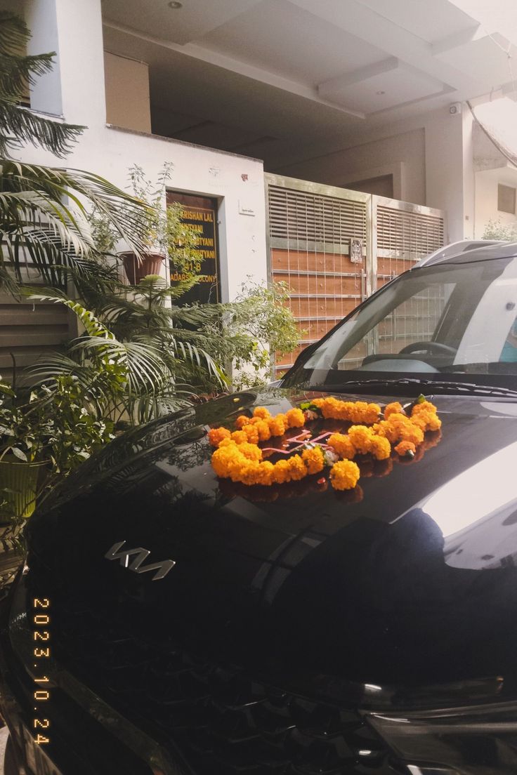 flowers are placed on the hood of a black car parked in front of a house