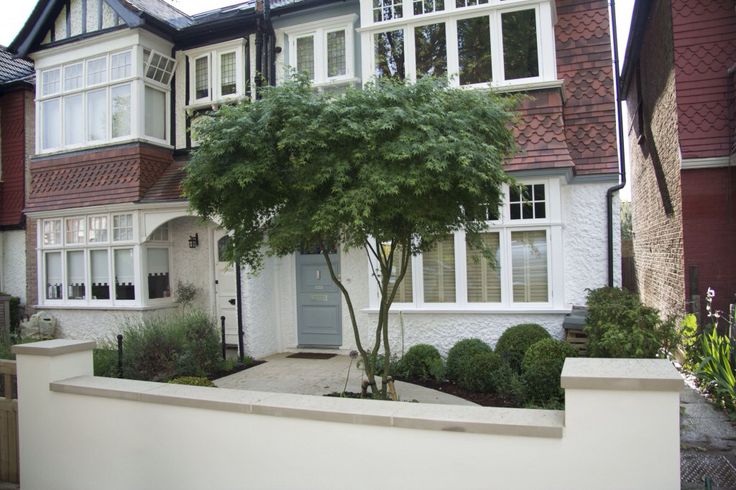 a white house with trees in front of it and bushes growing on the side of the building