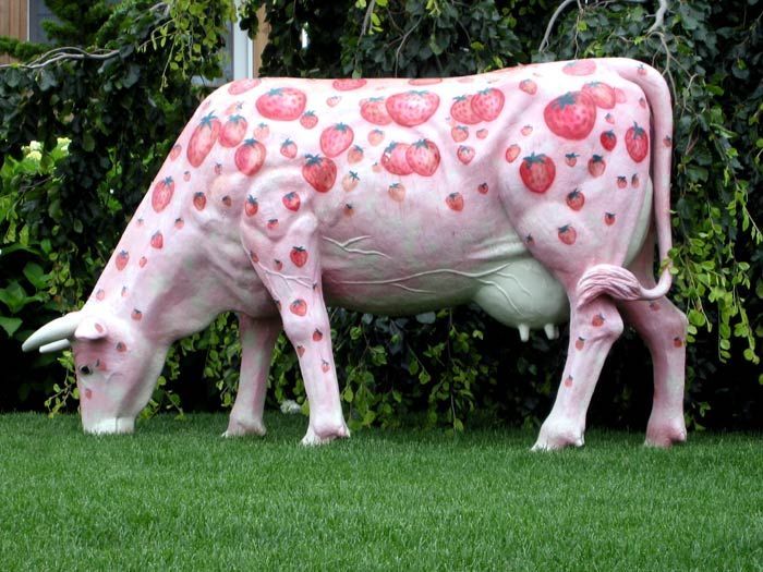 a statue of a cow with strawberries painted on it's body in the grass