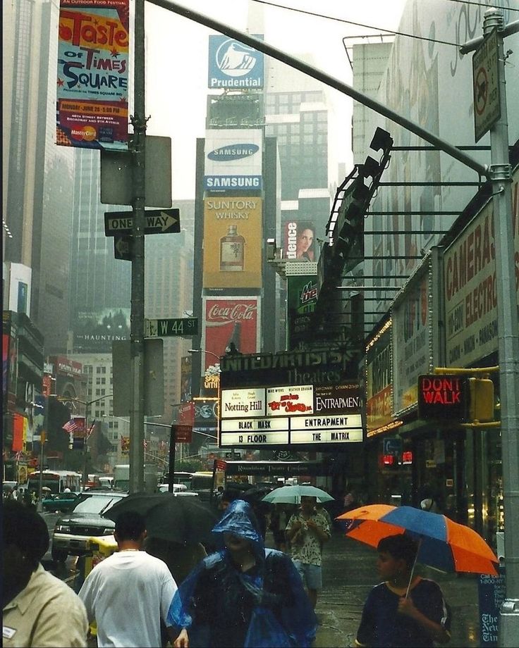 people are walking in the rain with umbrellas on a busy city street near tall buildings