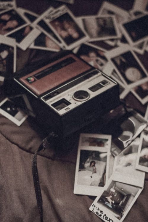 an old fashioned camera sitting on top of a bed covered in polaroid pictures and photos