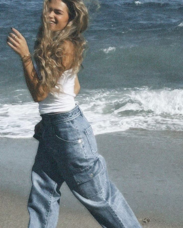 a woman standing on top of a beach next to the ocean holding a frisbee