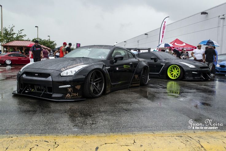 two black sports cars parked next to each other on a wet parking lot in the rain