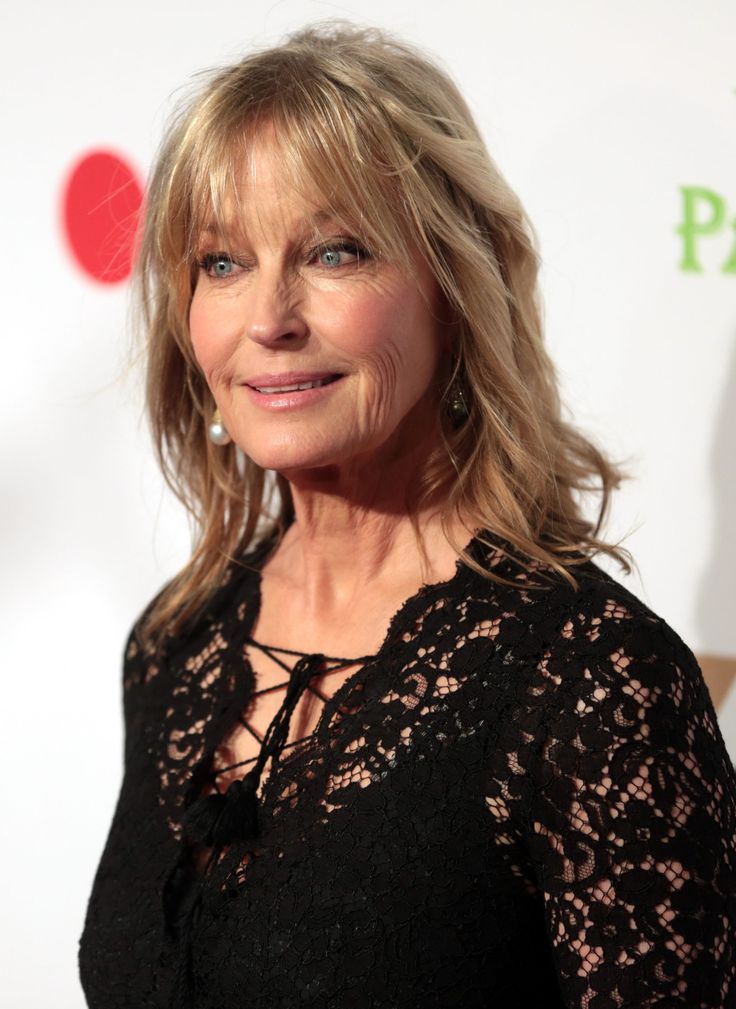 an older woman with blonde hair and blue eyes smiles at the camera while standing in front of a red carpet