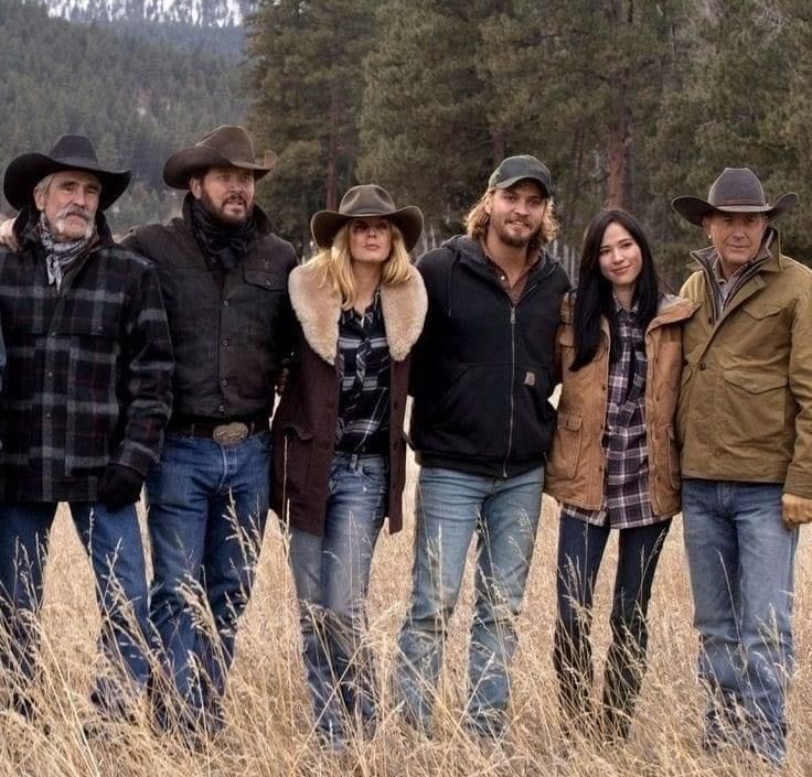 a group of people standing next to each other in a field with tall grass and trees