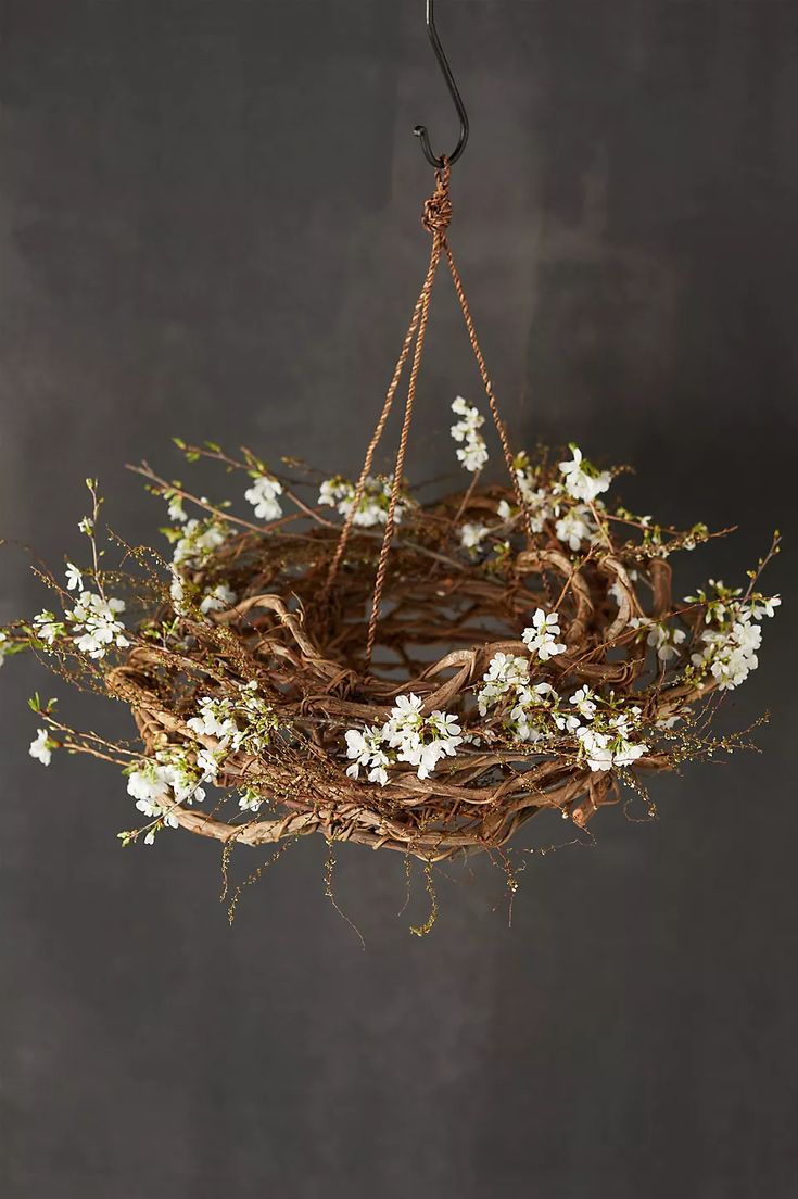 a bird nest hanging from a rope with white flowers on the front and back branches