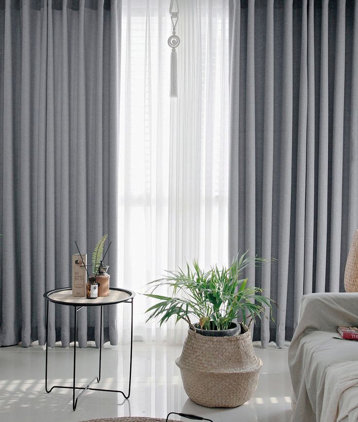 a living room filled with furniture and a large window covered in grey curtained drapes