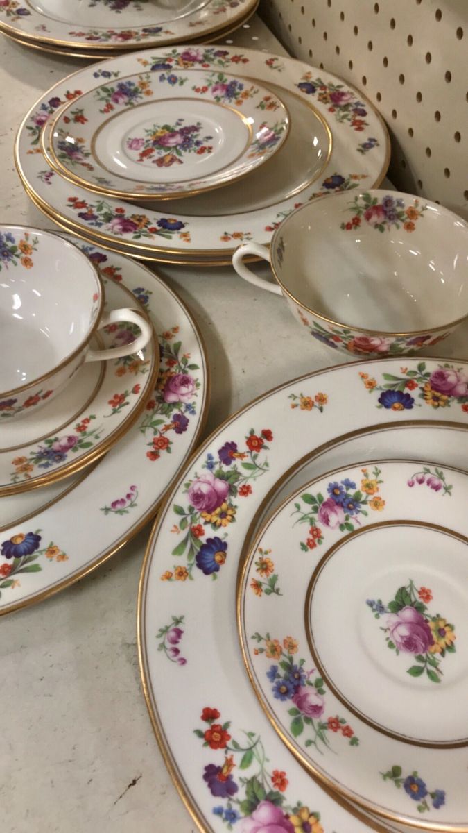 a table topped with lots of white and gold plates covered in flowered designs on it