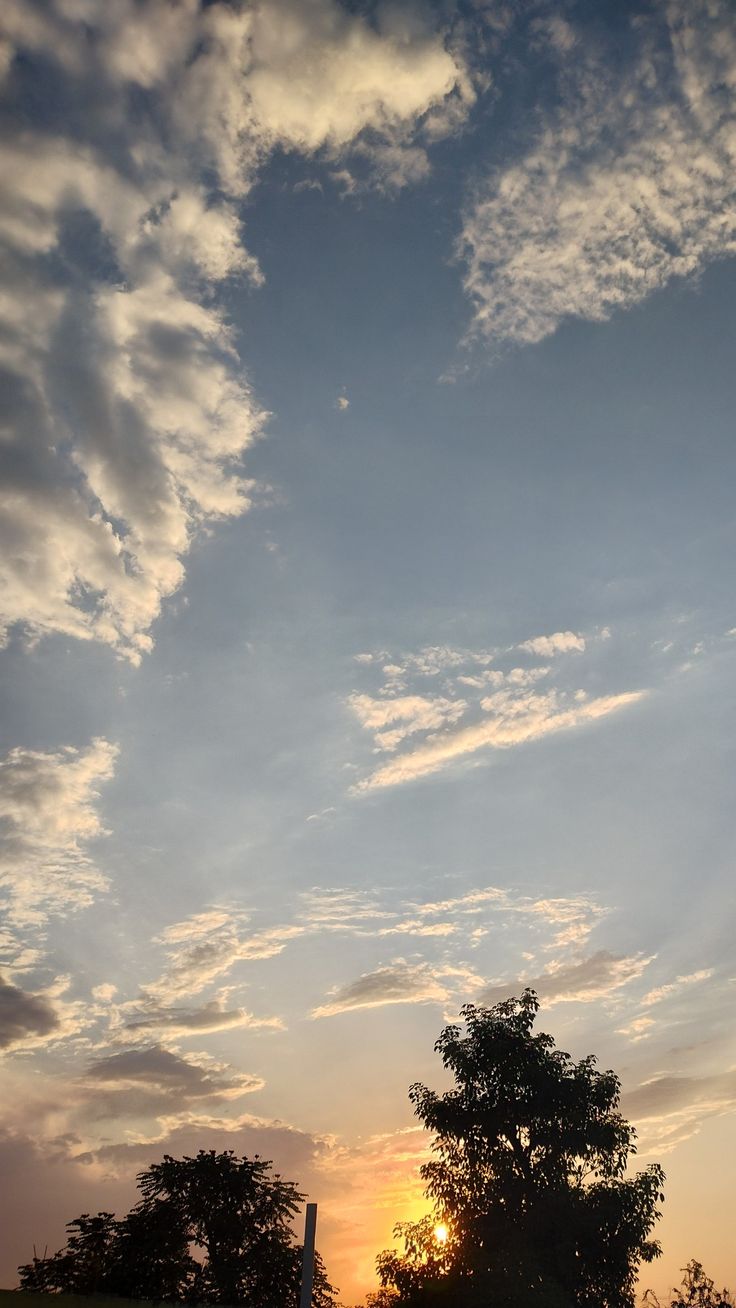 the sun is setting behind some clouds in the sky over a grassy field with trees