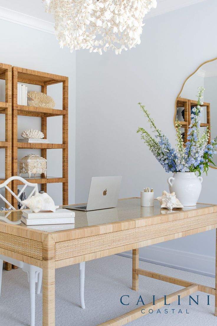 a wooden desk topped with a laptop computer next to a white vase filled with flowers