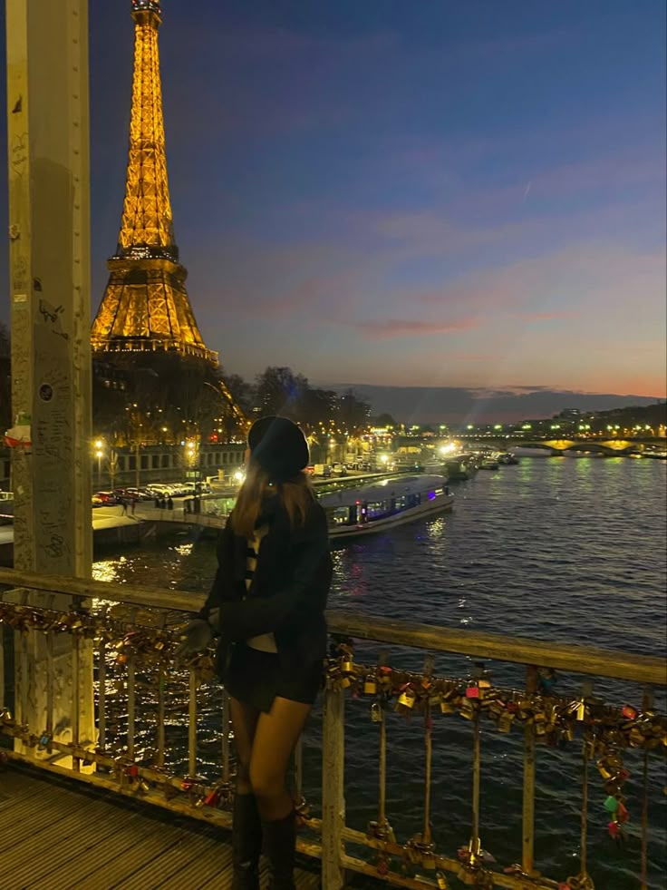 a woman standing on top of a bridge next to the eiffel tower at night