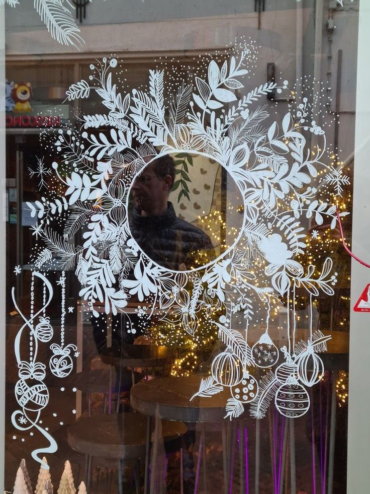 the reflection of a man standing in front of a window with christmas decorations on it