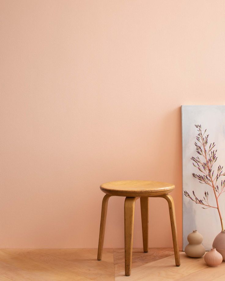 a small wooden stool next to a pink wall