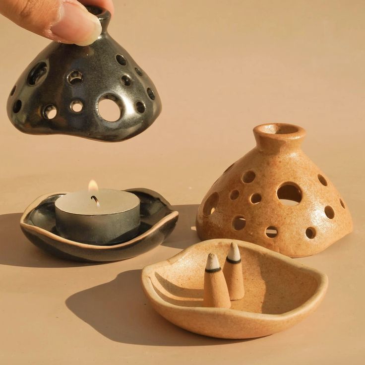 a person is holding a candle in front of some ceramic objects on a table top