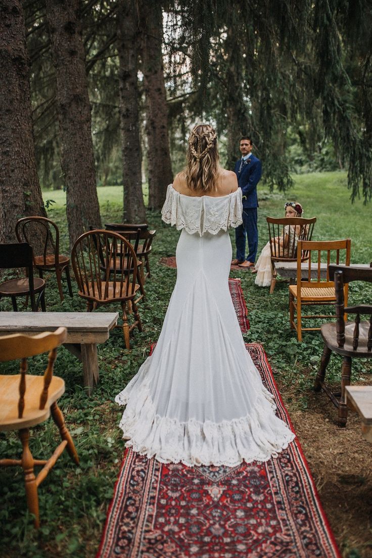 the back of a bride's dress as she walks down an aisle with chairs