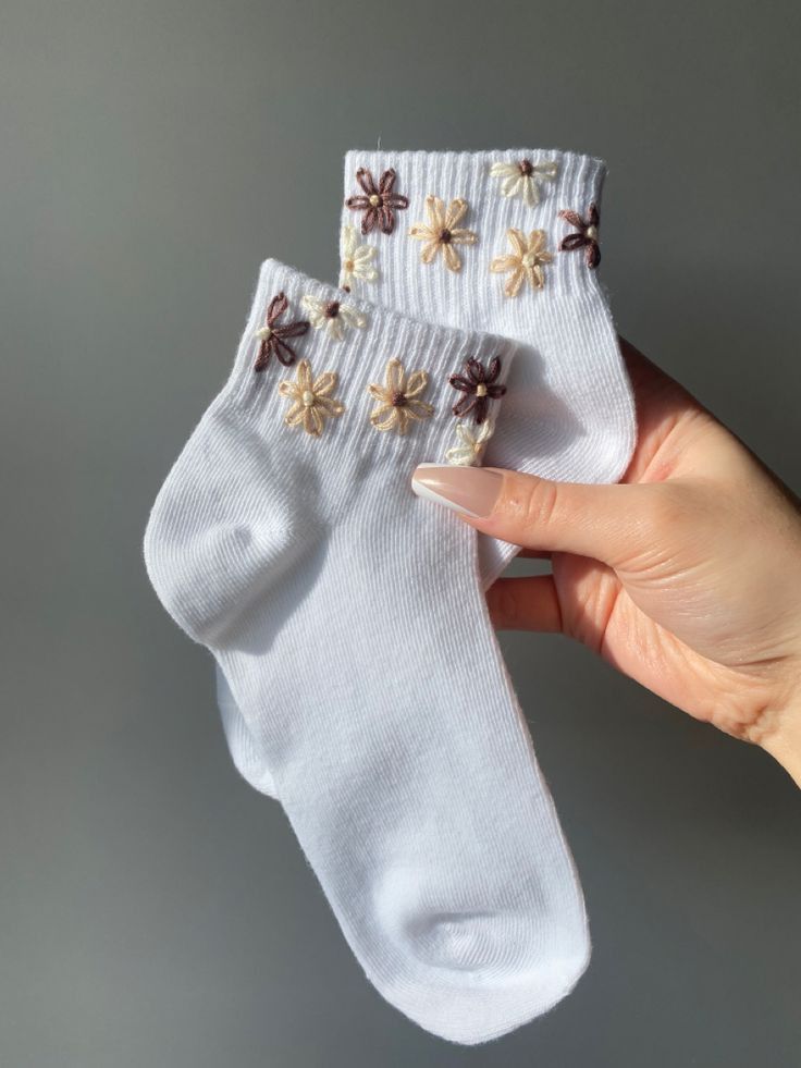 someone holding two pairs of white socks with flowers on the bottom, and one pair of brown