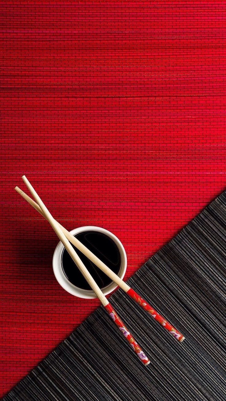 two chopsticks resting next to a cup of coffee on a red tablecloth