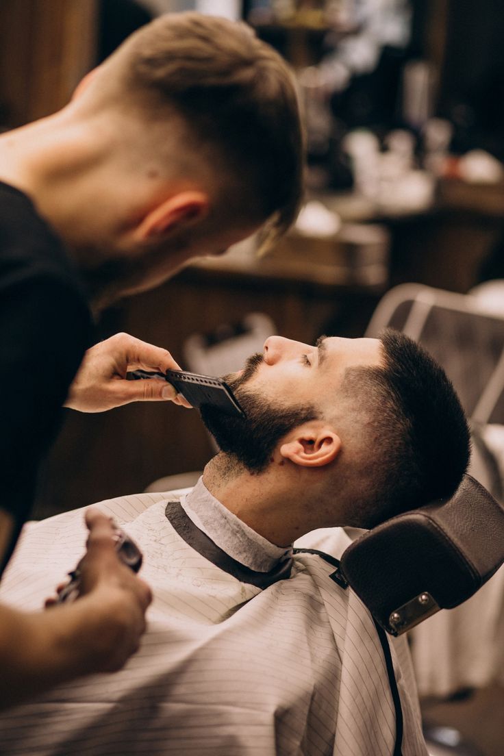 a man getting his hair cut by another man in a barbershop with scissors