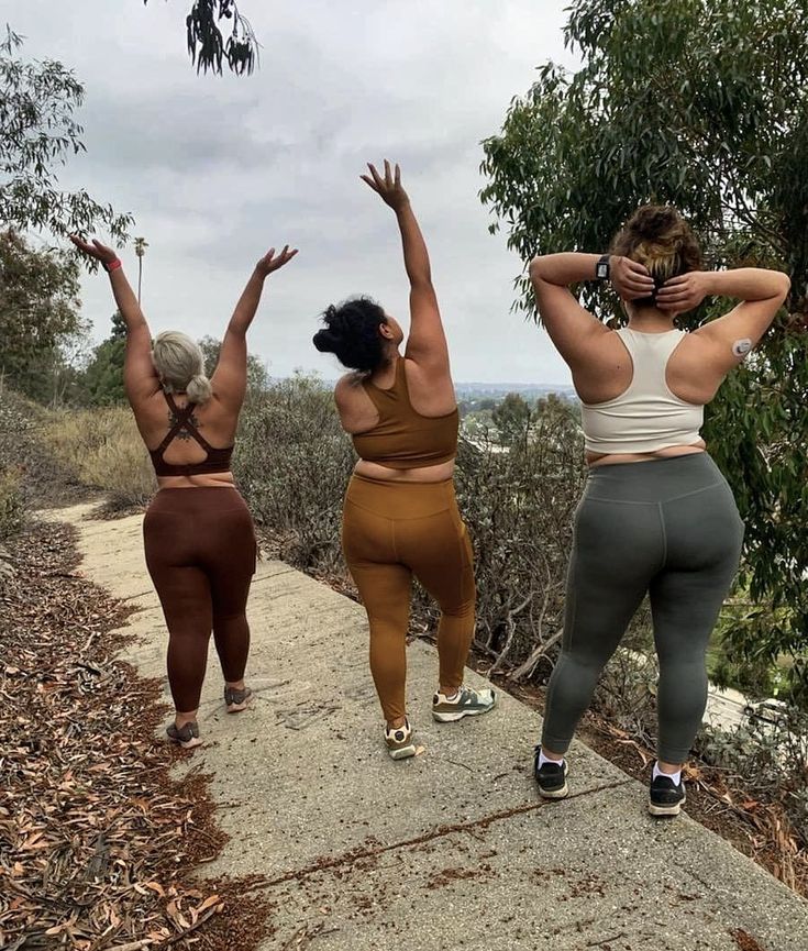 three women are walking down a path and one is holding her hands up in the air