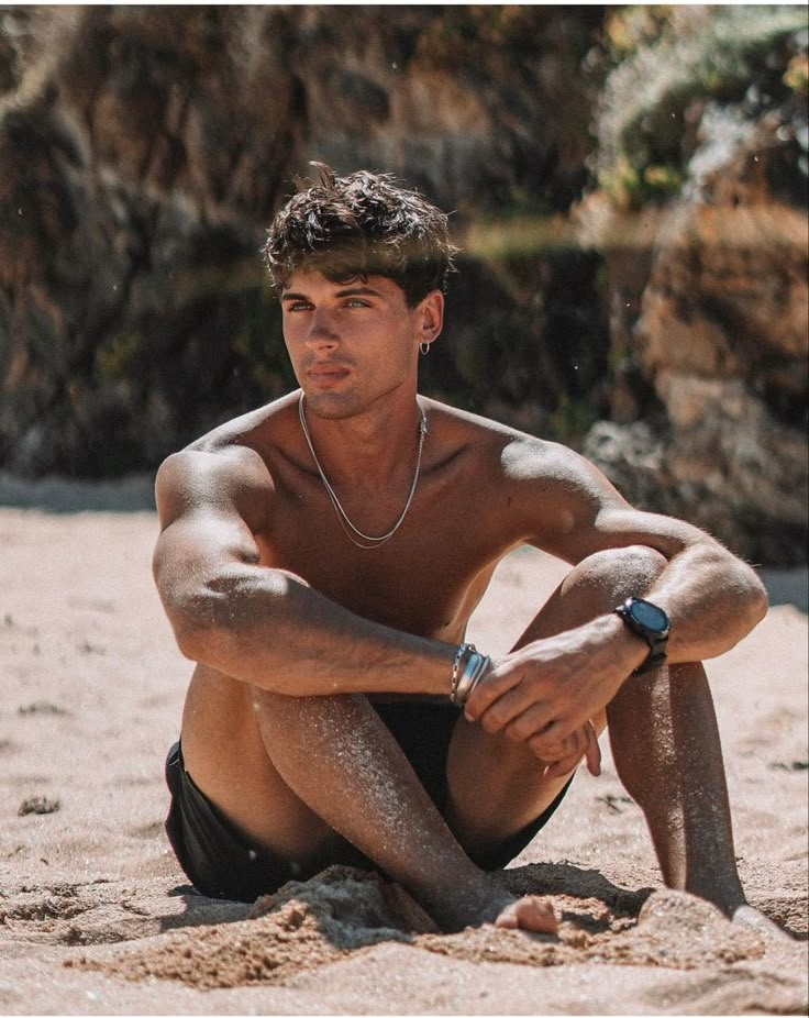 a man sitting in the sand with his hands on his knees