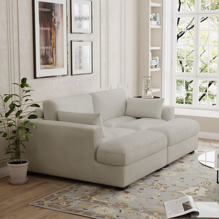 a living room with a white couch and large window in the corner, next to a potted plant