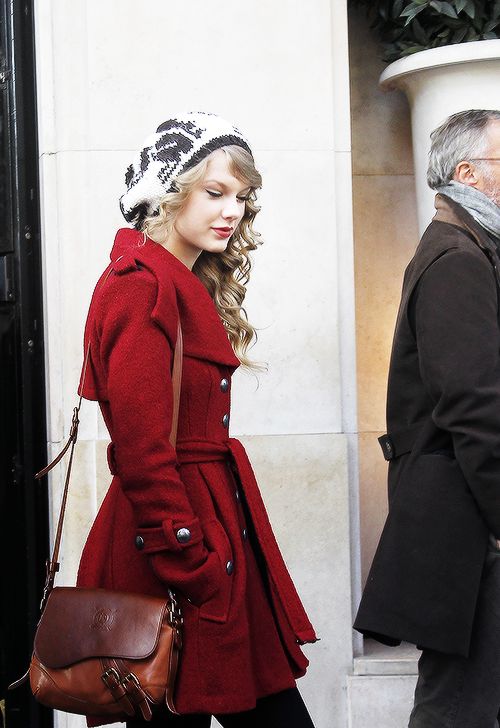 a woman in a red coat and hat is walking down the street with her handbag