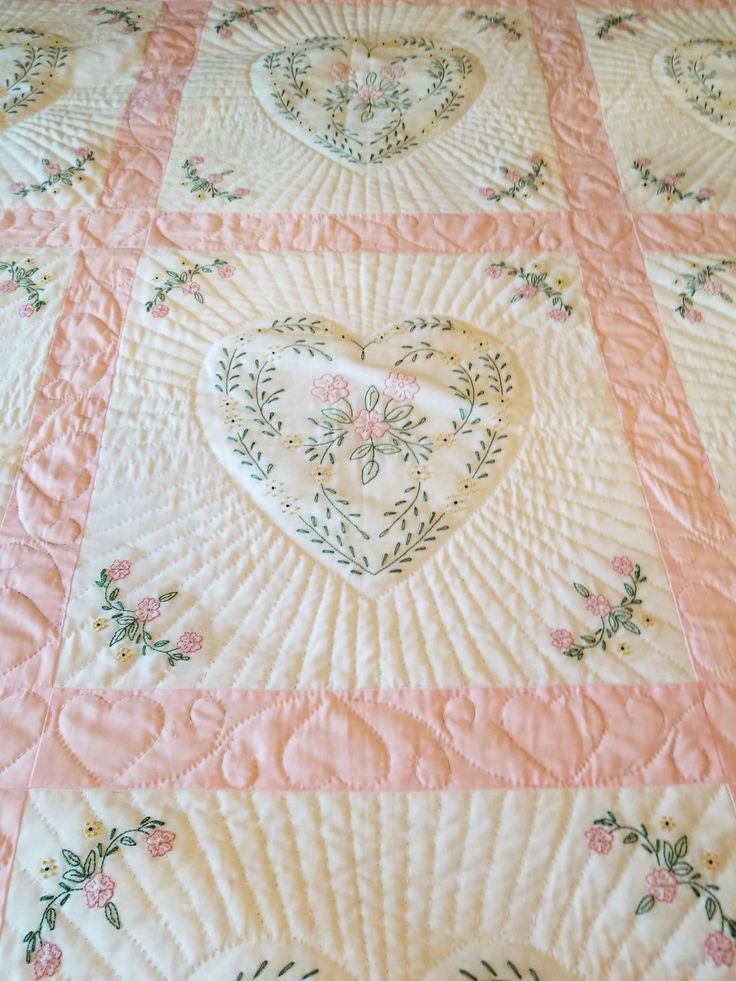 a quilted bed with pink and white hearts on it's side, in the shape of a heart