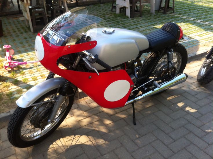 a red and white motorcycle parked on top of a brick road next to a sidewalk