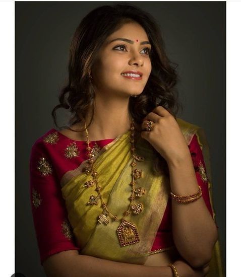 a woman in a red and yellow sari with gold jewelry on her neck, posing for the camera