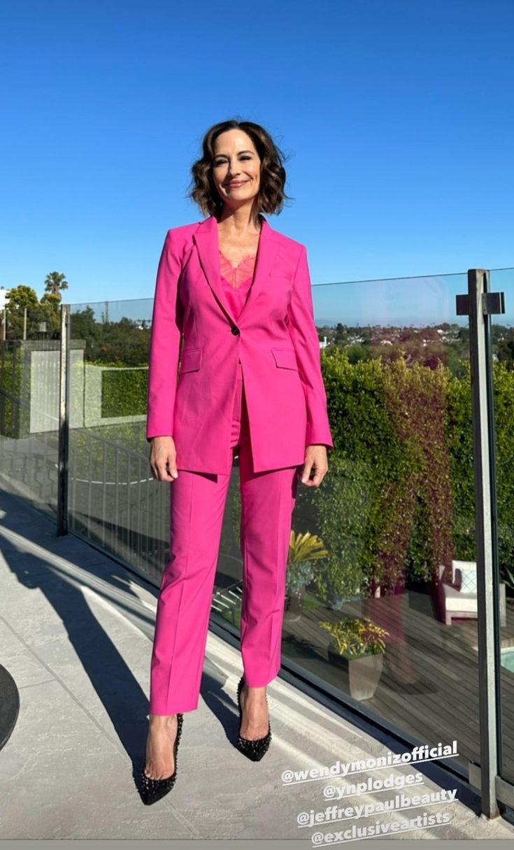 a woman in a pink suit standing on a balcony with her hands in her pockets