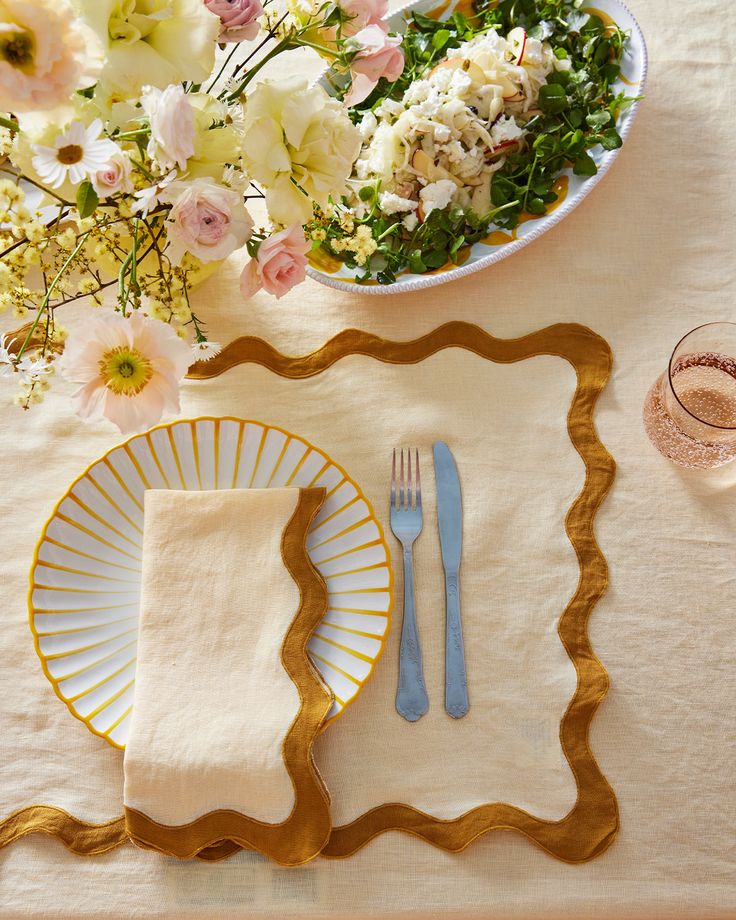 a place setting with flowers, napkins and glasses on top of a white table cloth