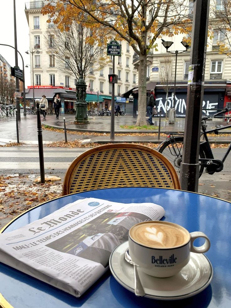 a cup of coffee sitting on top of a blue table next to a newspaper and some leaves