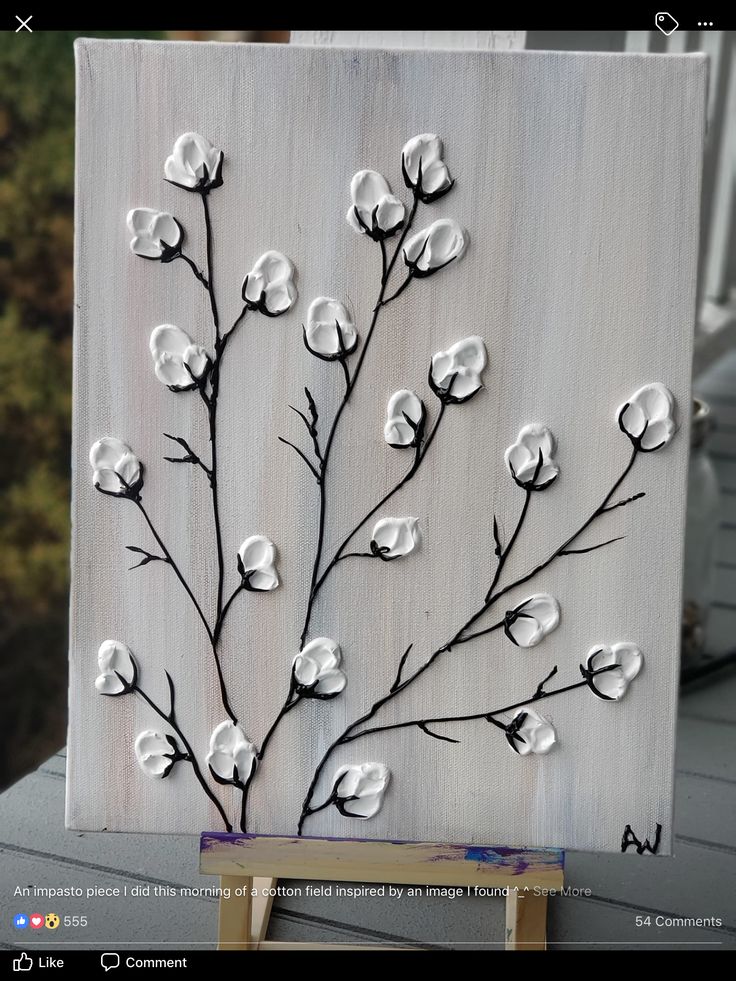 a painting with white flowers on it sitting on top of a wooden easel