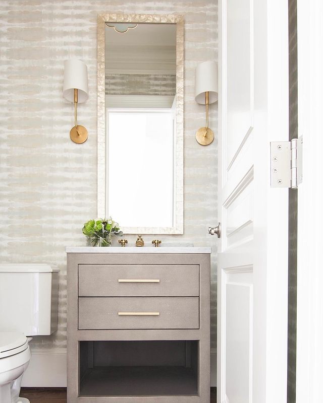 a white toilet sitting next to a bathroom sink under a mirror on top of a wooden cabinet