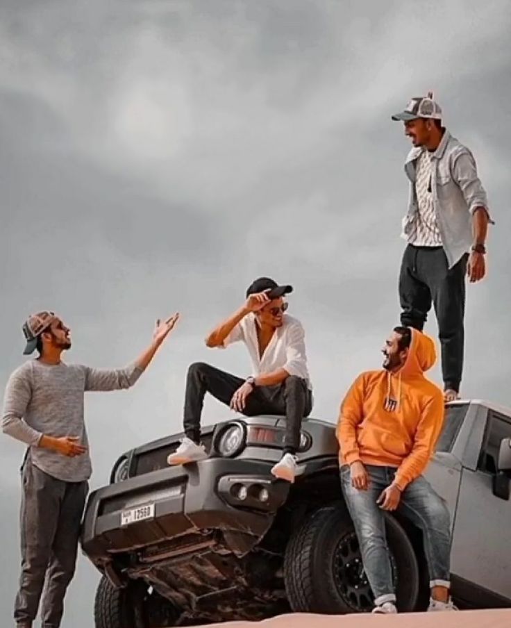 four men are sitting on top of a jeep in the desert, one man is pointing at something