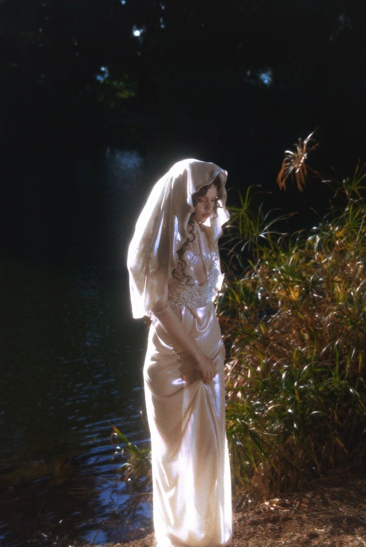 a woman dressed in white standing next to a body of water