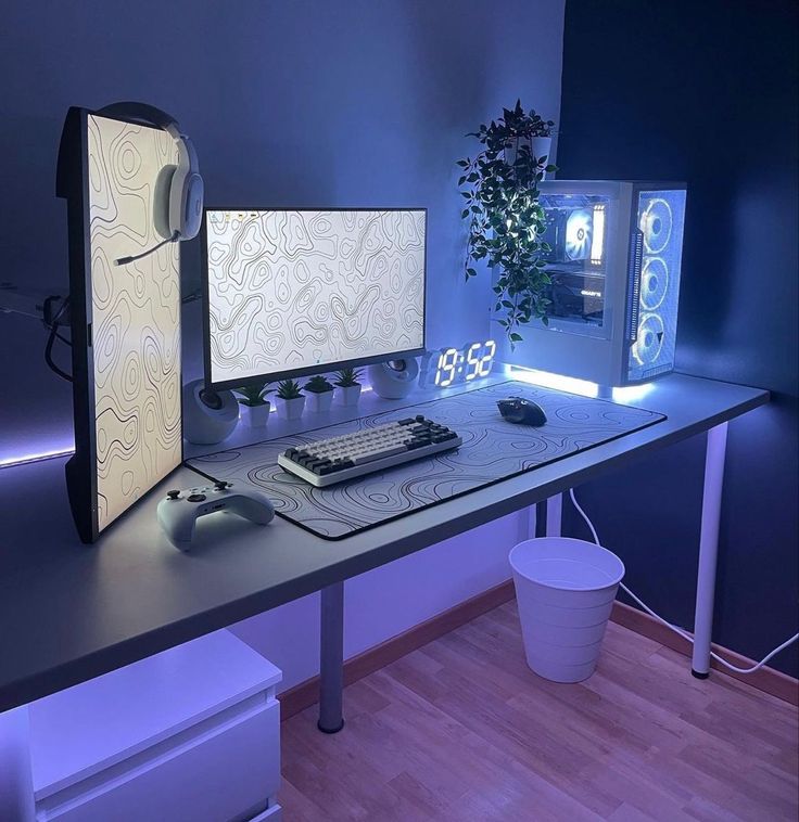 a computer desk with two monitors and a keyboard on it in front of a potted plant