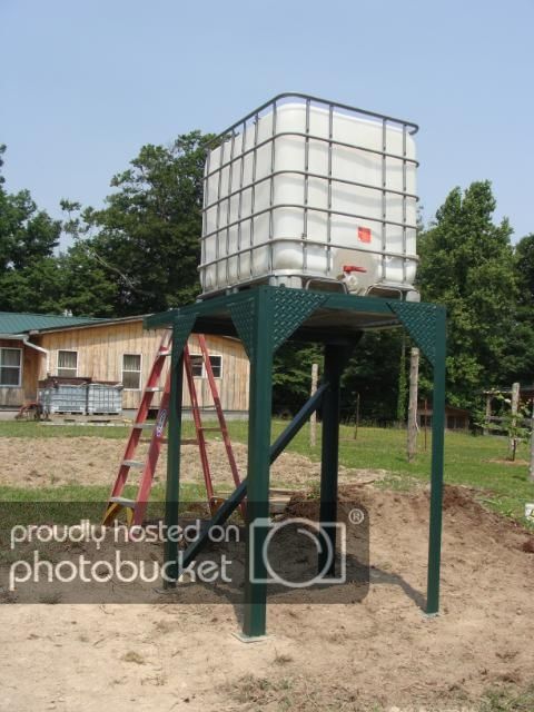 a large metal water tank sitting on top of a green stand in the middle of a field