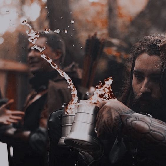 a man with long hair pouring something out of a metal cup into another person's hand