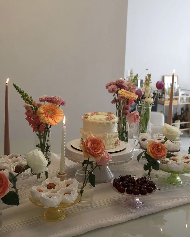 a table topped with cakes and flowers on top of it's countertop next to candles