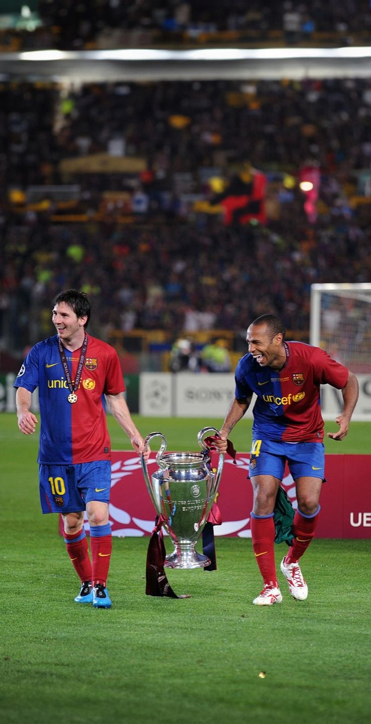 two soccer players walking on the field with a trophy in his hand and another player standing next to him