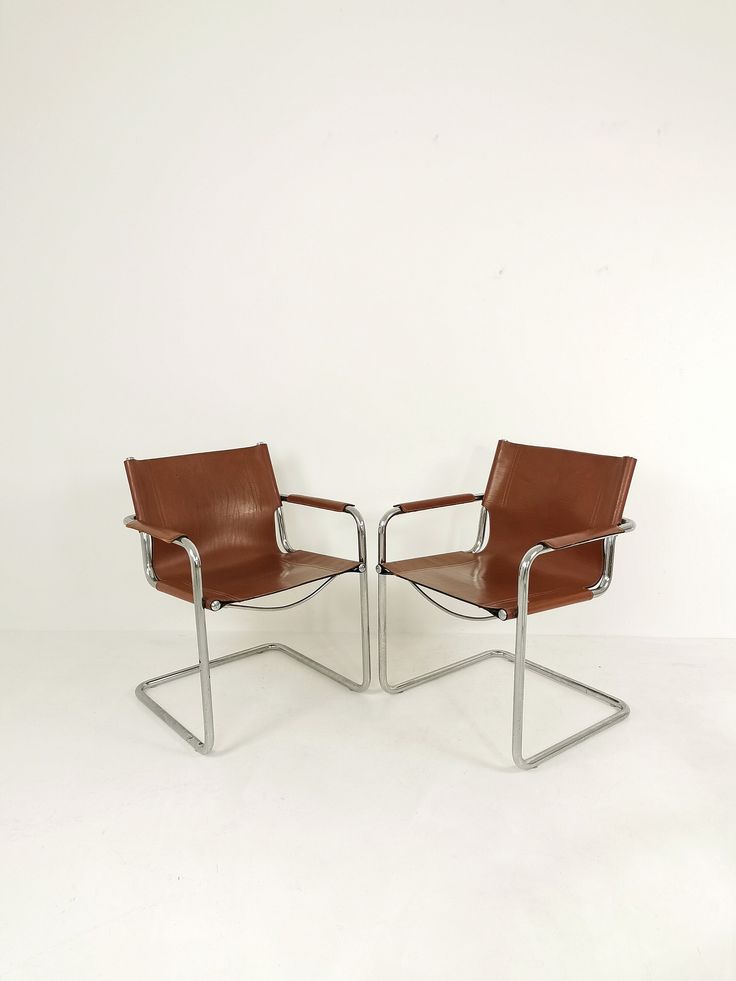 two brown leather chairs sitting next to each other on a white floor in front of a wall